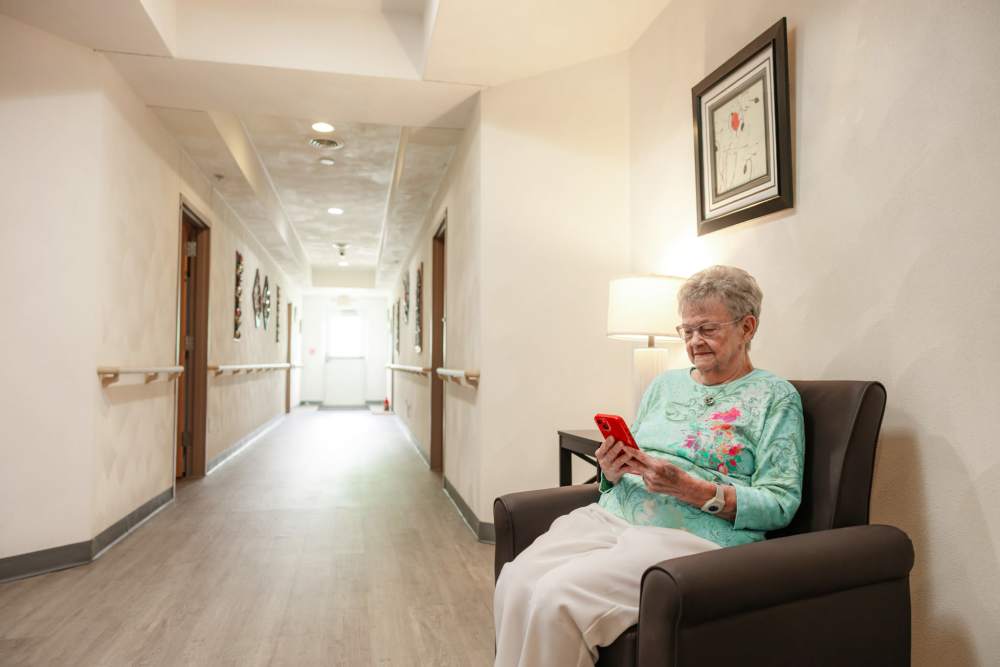 Elderly person seated in hallway holding red smartphone at Garden Place Millstadt in Millstadt, Illinois