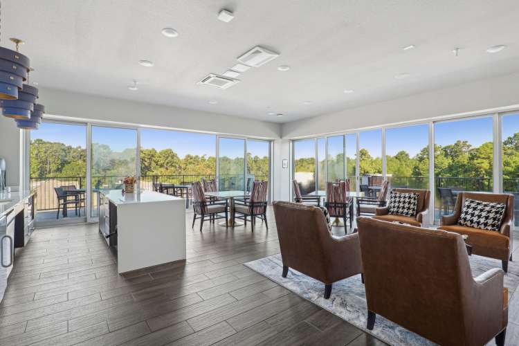 Spacious living room in an active adult community unit with large windows and a balcony view overlooking wooded scenery.