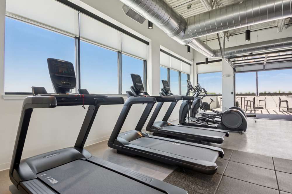 Modern gym with treadmills and elliptical machines by large windows at Tempo at Nine Mile Station in Aurora, Colorado