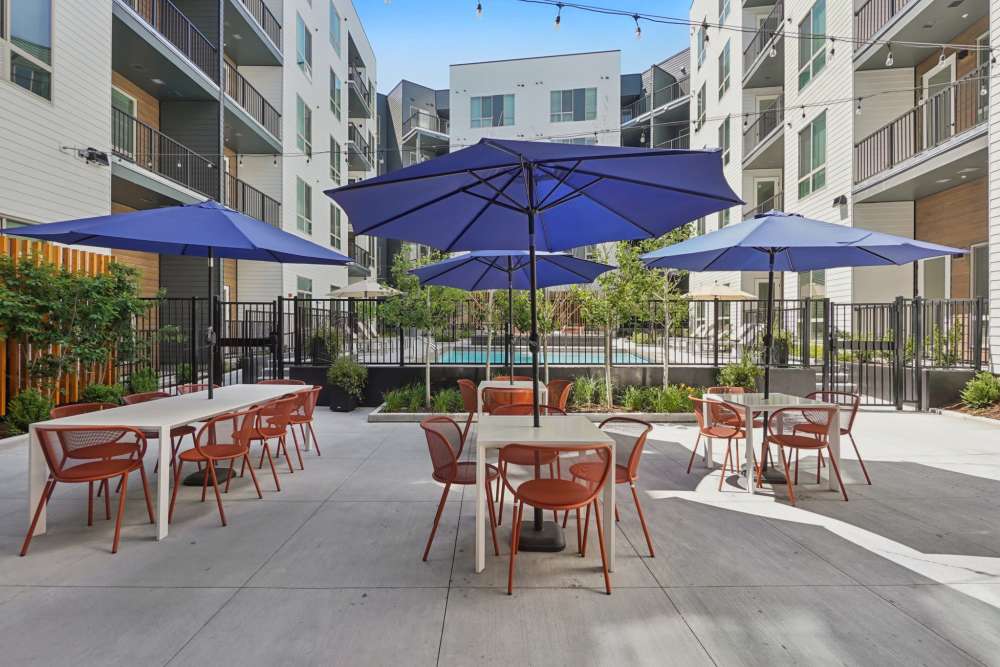 Outdoor seating area with orange chairs, blue umbrellas, and nearby pool at Tempo at Nine Mile Station in Aurora, Colorado