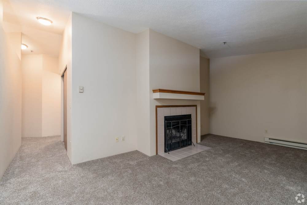Unfurnished living room with gray carpet and a fireplace with tiled surround and wooden mantel at Stonecrest Apartments in Spokane, Washington