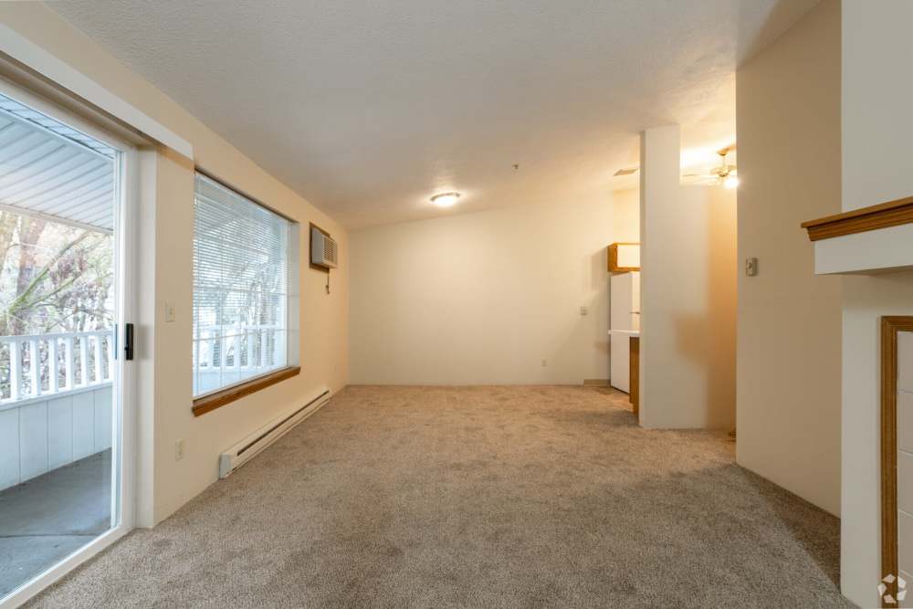 Unfurnished living room with beige carpet, sliding glass door to balcony and open kitchen area at Stonecrest Apartments in Spokane, Washington
