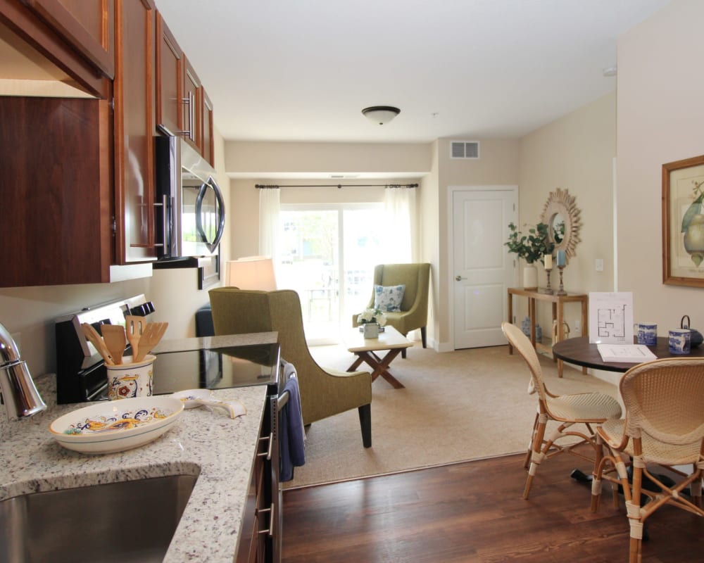 Resident kitchen with hardwood floors and carpeted living room at The Pillars of Hermantown in Hermantown, Minnesota