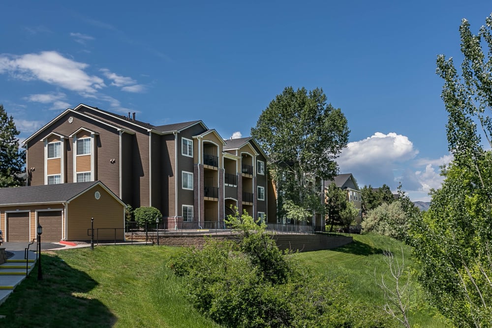 The building's exterior surrounded by a lush green landscape at The Crossings at Bear Creek Apartments in Lakewood, Colorado