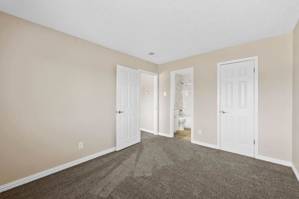 Carpeted bedroom with connecting bathroom and closet space at Village Square in Irving 