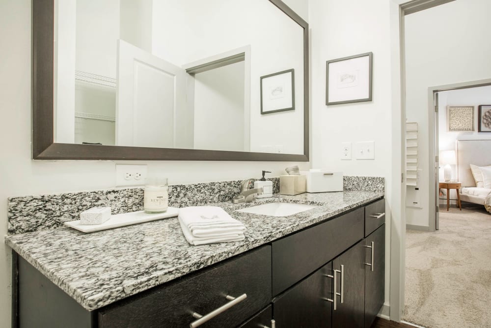 Master bathroom with large mirror, granite counter, and wood cabinets at Marq Midtown 205 in Charlotte, North Carolina