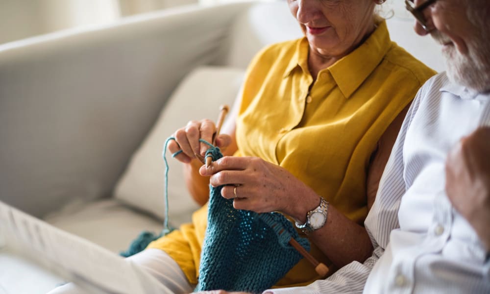 A resident knitting next to her husband on the couch at Randall Residence of Fremont in Fremont, Ohio