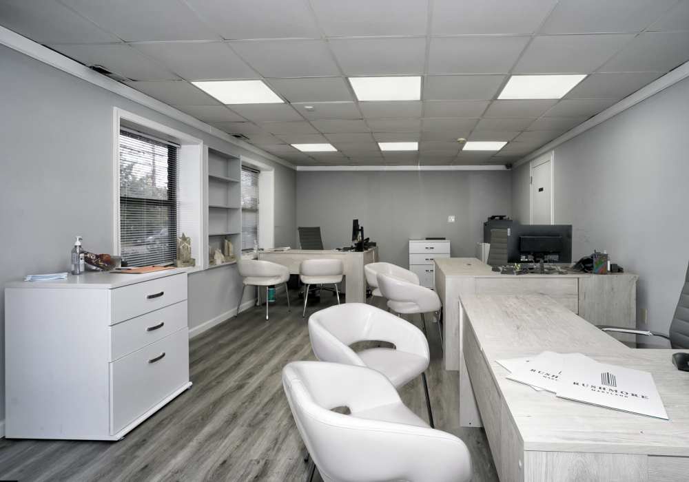 Bright office space with modern furniture, wood-style flooring, and large windows providing natural light at Dutch Village Apartments in Baltimore, Maryland