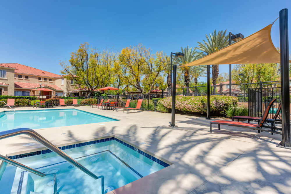 Spa and pool with lounge chairs and umbrellas at Tuscany Village Apartments in Ontario, California