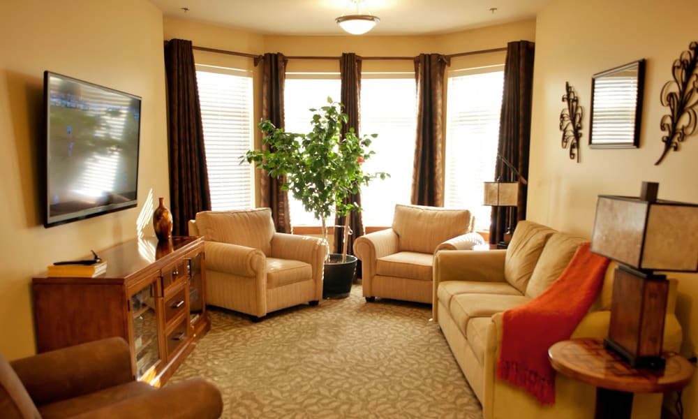 Senior apartment living room with chairs and a couch arranged opposite a tv mounted on the wall at Fair Oaks Health Care Center in Crystal Lake, Illinois