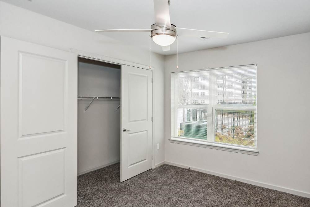 A view of an unfurnished bedroom with access to the walk-in closet and a ceiling fan at Flats at Mount Zion in Stockbridge, Georgia