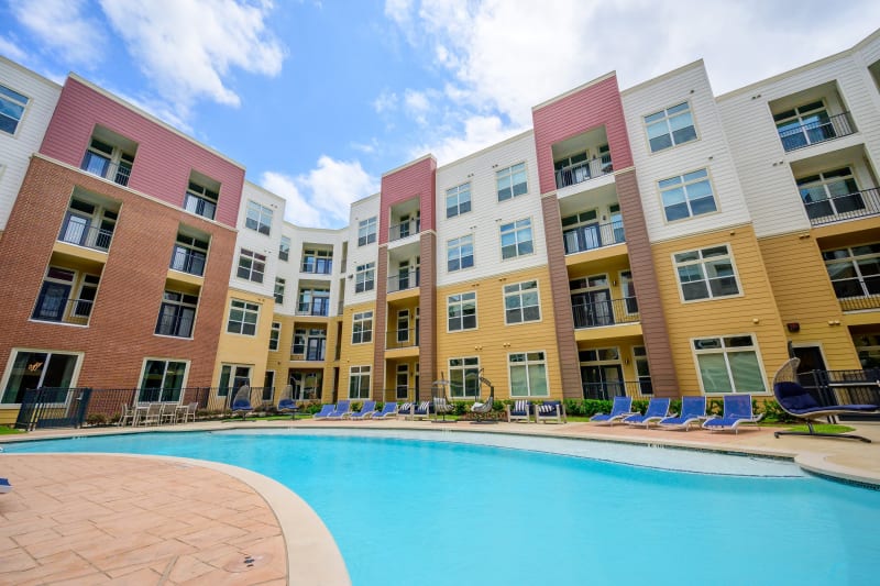 Resort-style swimming pool surrounded by chaise lounge chairs and mature trees at Aspire at 610 in Houston, Texas