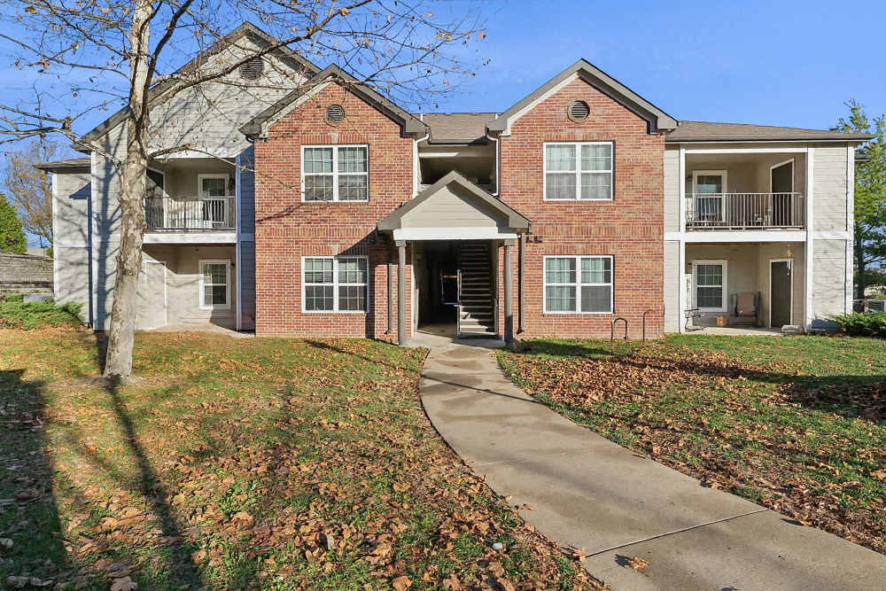 Charming apartment entrance at Covington Woods Apartments in Lansing, Kansas surrounded by lush landscaping and a welcoming path.
