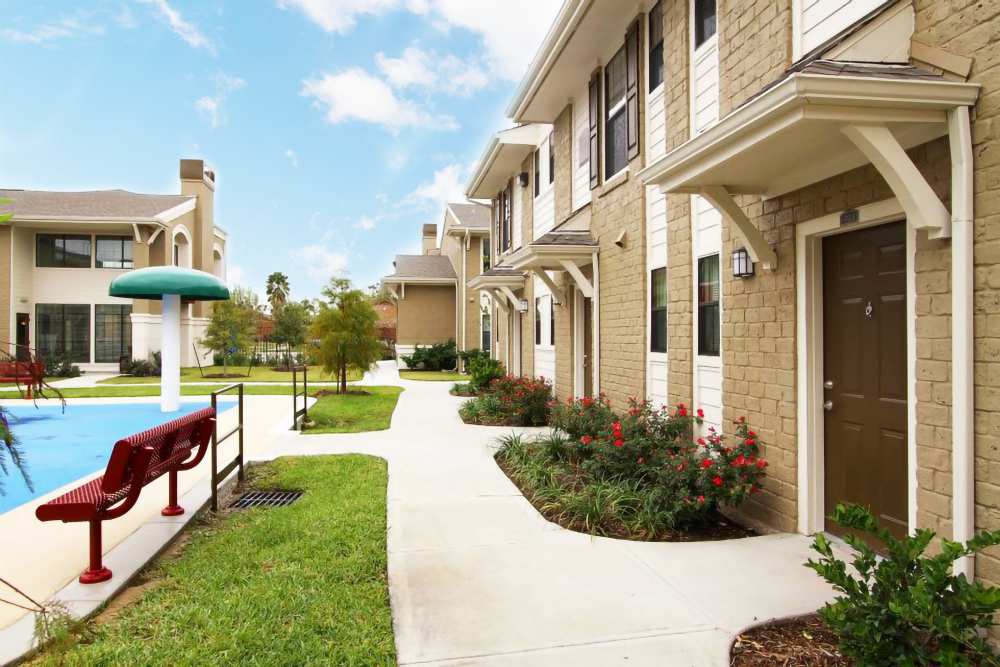 Landscaped pathways with poolside view and apartment building exterior at Villa Del Prado in Houston, Texas