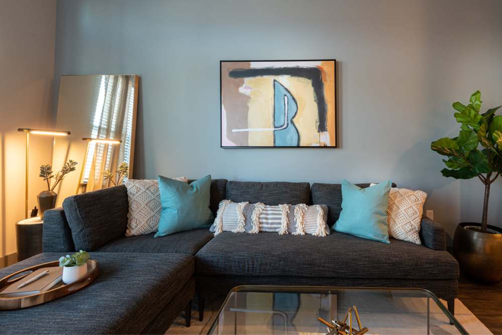Living room setup with dark gray sectional sofa, decorative pillows, abstract wall art, and indoor plants for added greenery at The Reserve at Patterson Place in Durham, North Carolina