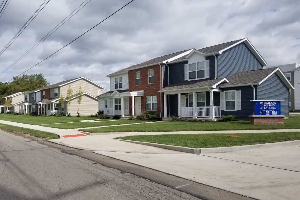 Two-story apartment buildings with landscaped lawns and sidewalks, inviting front porches and a community sign at Wheatland Crossing II in Columbus, Ohio