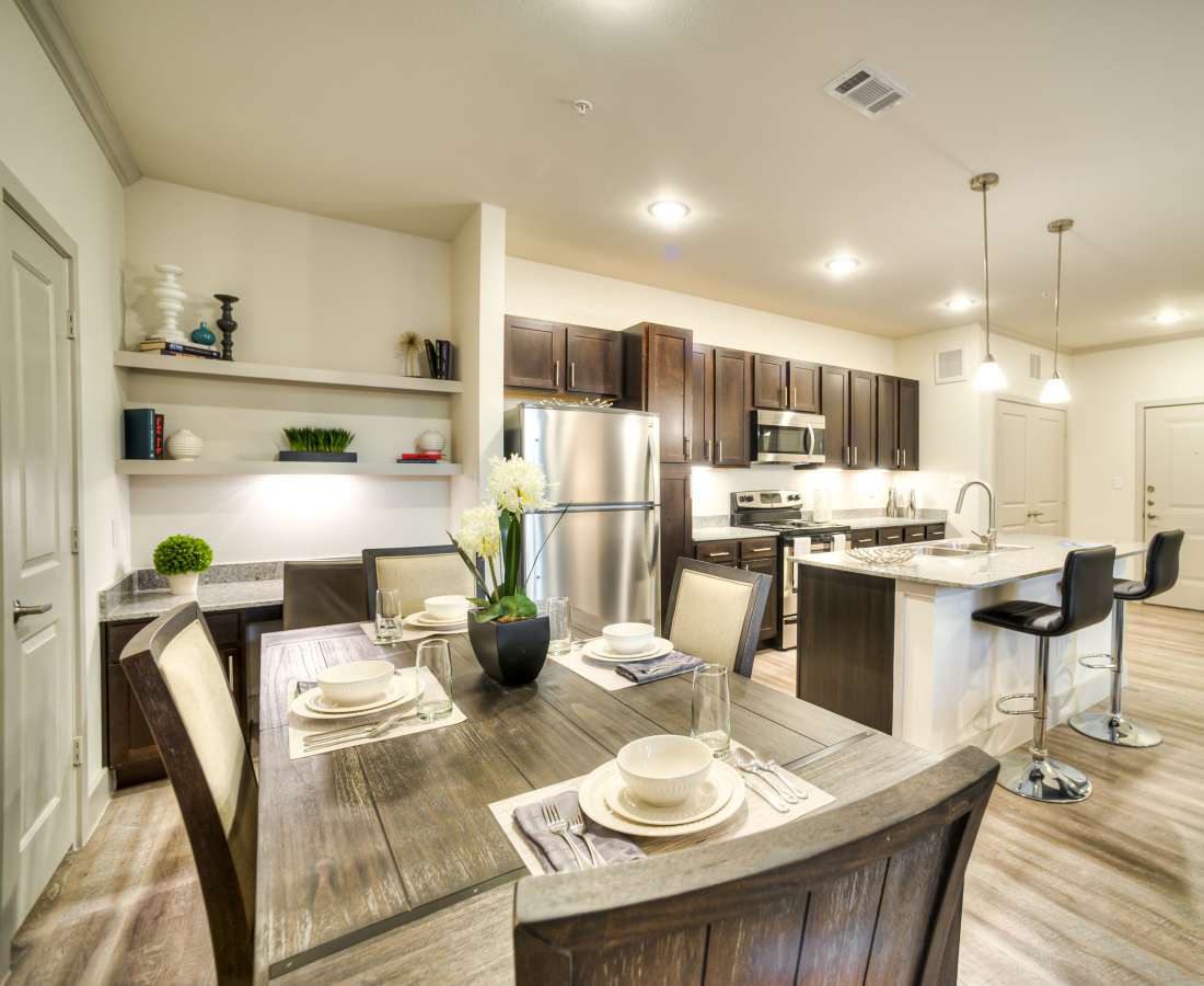Modern kitchen with granite countertops, stainless steel appliances, and wood-style flooring, dining area with table and chairs at Magnolia Park Apartments in Houston, Texas