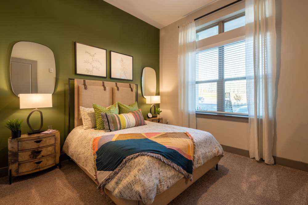 Cozy bedroom with green accent wall, large window, and modern decor including framed artwork above the bed at The Reserve at Patterson Place in Durham, North Carolina