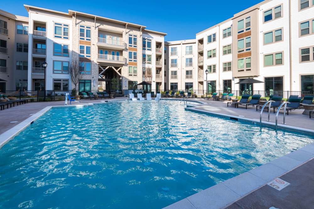 Expansive resort-style swimming pool with built-in loungers and surrounding seating areas near multi-story apartment buildings at The Reserve at Patterson Place in Durham, North Carolina.
