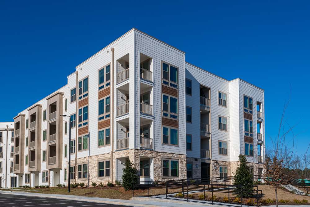 Modern multi-story apartment building with white and beige exterior, large windows, and private balconies under a clear blue sky at The Reserve at Patterson Place in Durham, North Carolina.