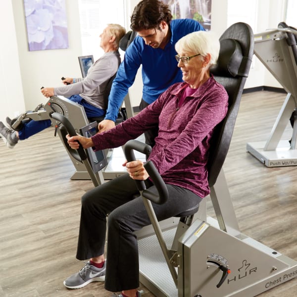 Gym instructor assisting a resident on a workout machine at Quail Park at Shannon Ranch in Visalia, California