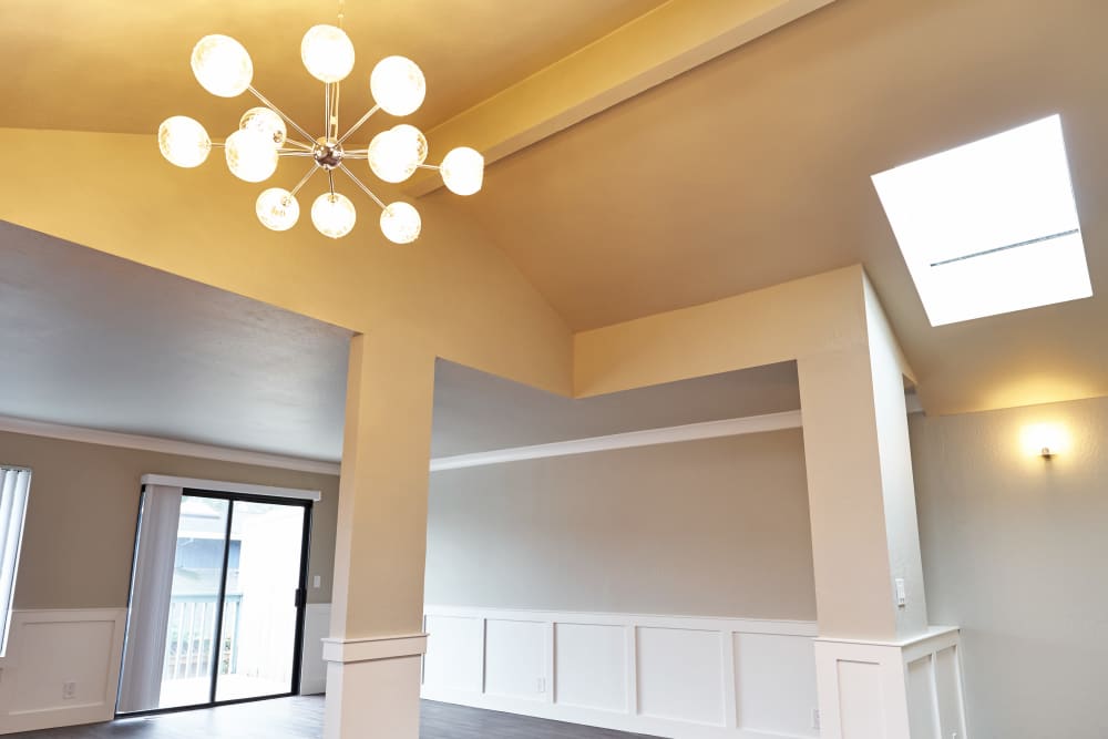 Modern room with high ceilings, chandelier with spherical lights, large windows, sliding glass doors, skylight, and neutral-colored walls with wainscoting. at Santa Cruz Coast Homes in Santa Cruz, California