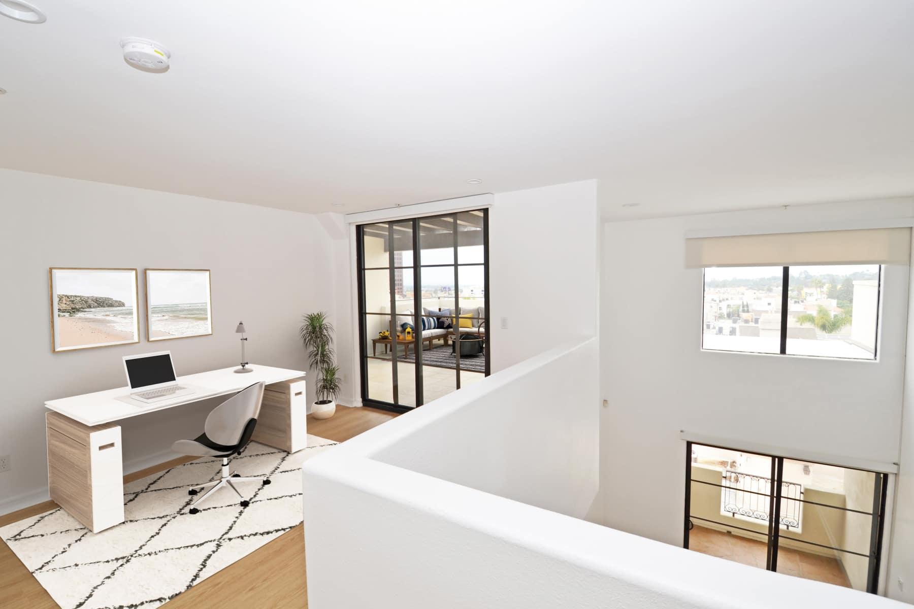 Home office with white desk, swivel chair, laptop, beach-themed art, and balcony access at Luxe Villas in Brentwood, California