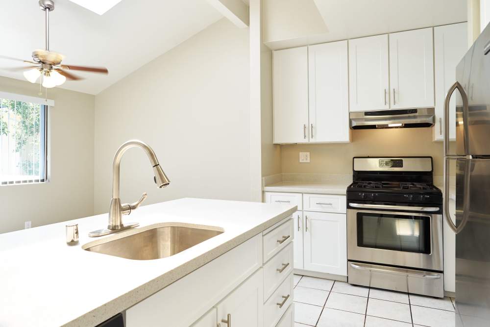 Modern kitchen featuring white cabinets, stainless steel appliances, white countertops with integrated sink, and a ceiling fan with lights. at Santa Cruz Coast Homes in Santa Cruz, California
