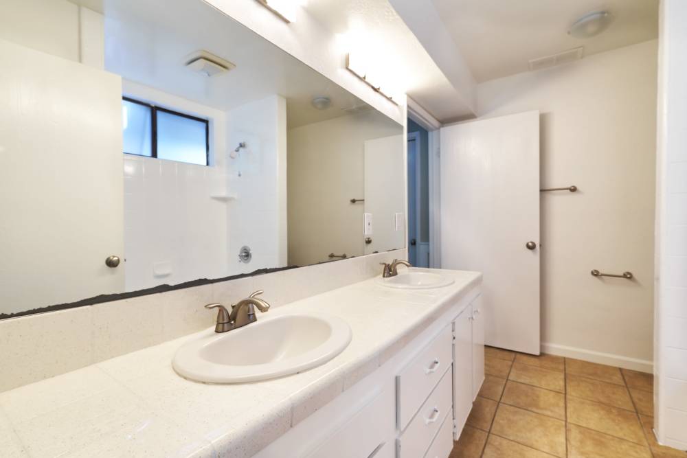 Modern bathroom with white countertop and single sink, large mirror, tiled flooring, natural light from window, and wall-mounted towel racks. at Santa Cruz Coast Homes in Santa Cruz, California