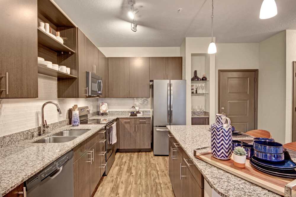 Kitchen with dishwasher, refrigerator, wood cabinet and granite countertop at The Courtney at Lake Shadow in Orlando, Florida 