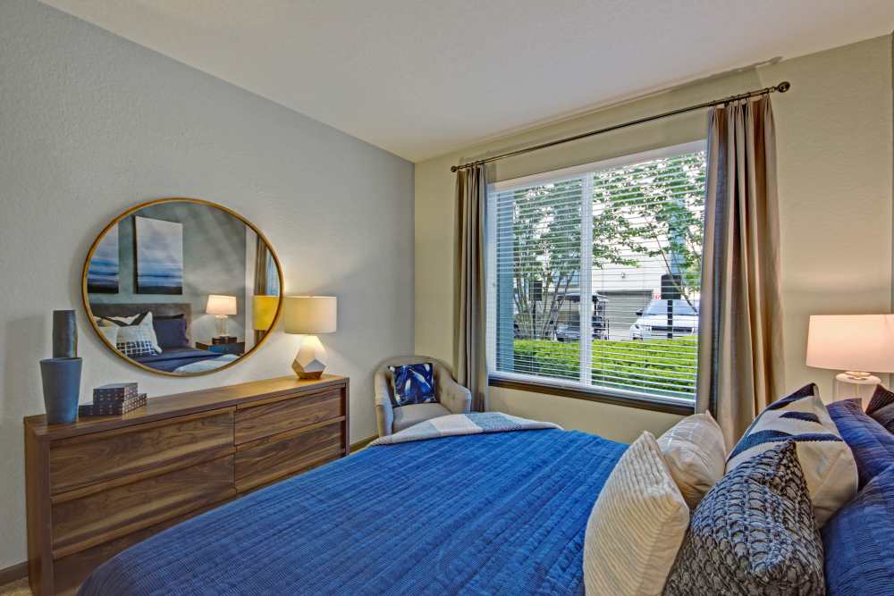 Model bedroom with large bed, round mirror and large window at The Courtney at Lake Shadow in Orlando, Florida