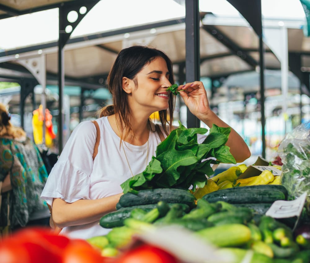 Resident smelling fresh herbs at an open-air farmers market near Domus on the Boulevard in Mountain View, California