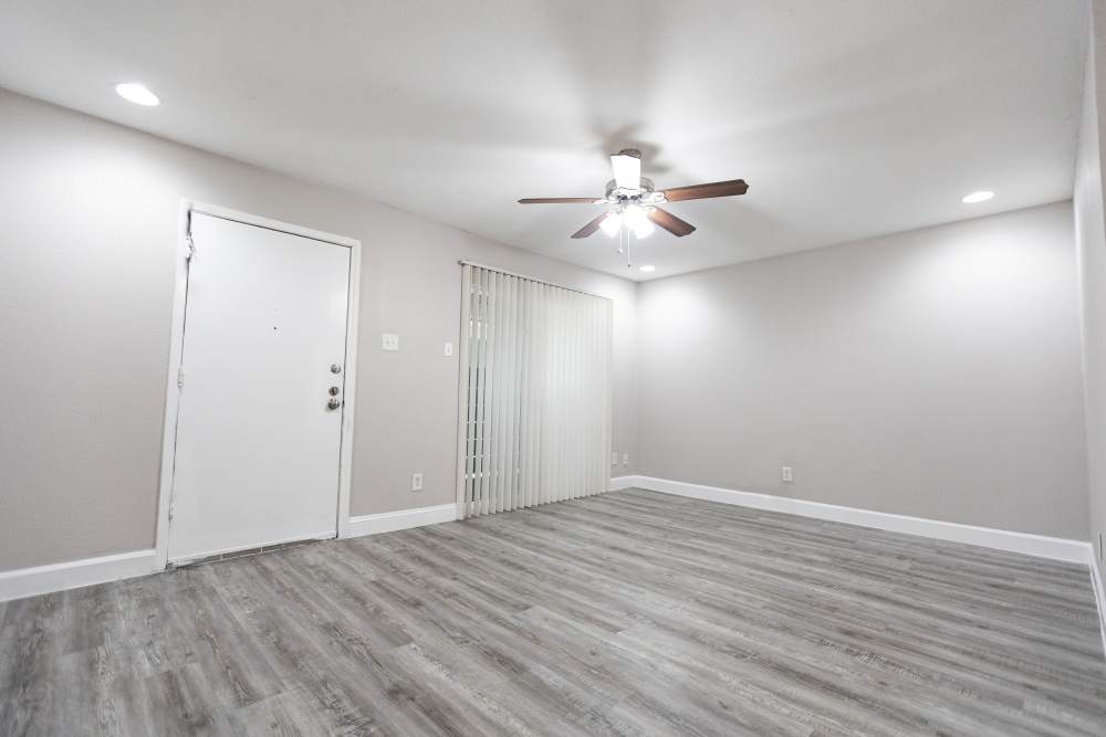 Spacious, light-filled living area with stylish grey flooring and modern ceiling fan at San Mateo Forest in Dallas, Texas.