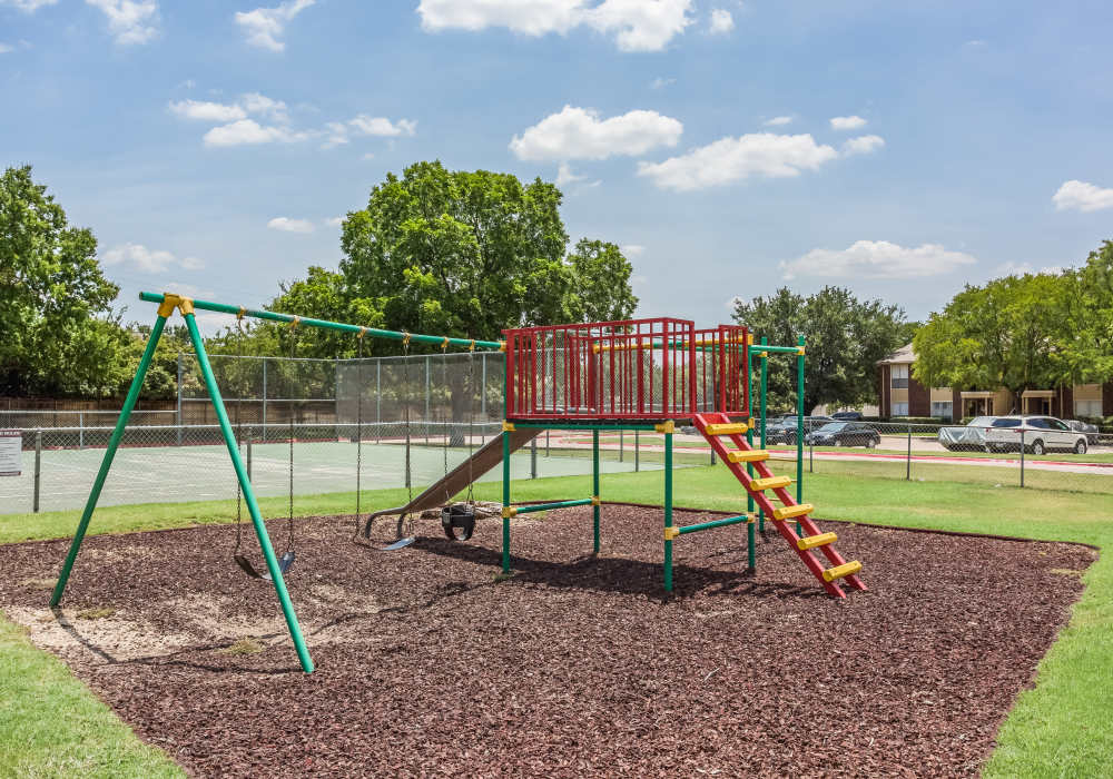 Charming playground with vibrant swings and a climbing structure, surrounded by lush landscaping at Charter Oak in Euless, Texas.