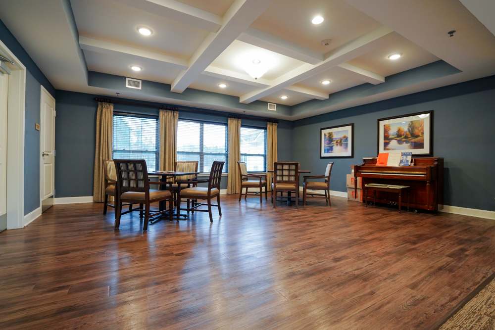 A sitting area arranged with round tables, chairs and a piano placed against the wall at The Harmony Collection at Columbia in Columbia, South Carolina