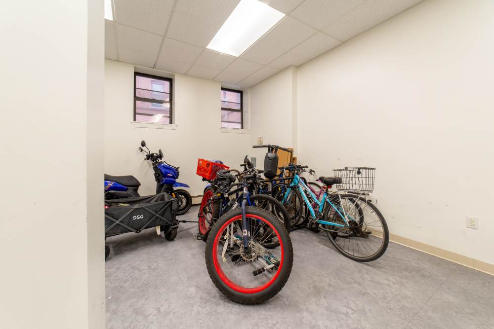 Bicycle storage area with various bikes and scooters against white walls and windows at 15-25 Hemenway Apartments in Boston, Massachusetts