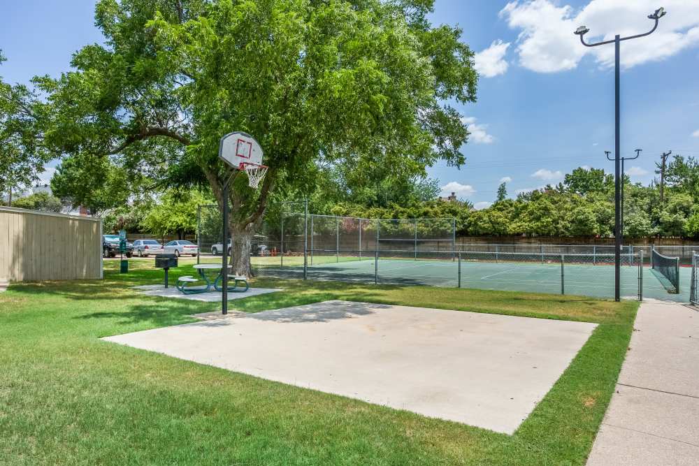Recreational oasis with a basketball court and tennis courts surrounded by lush landscaping at Charter Oak in Euless, Texas.