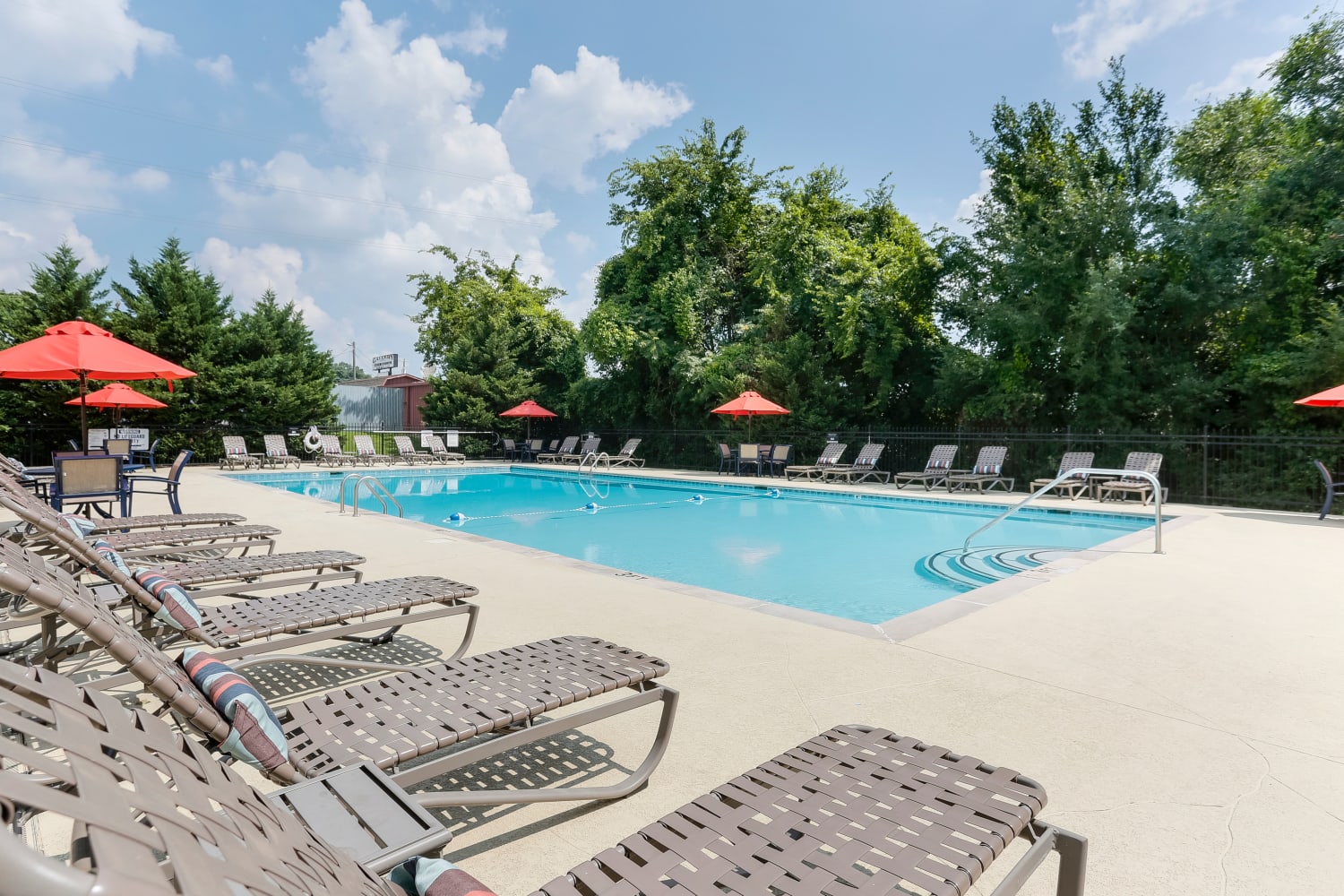 Swimming pool surrounded by lounge chairs and patio tables with umbrellas at Jackson Grove Apartment Homes in Hermitage, Tennessee