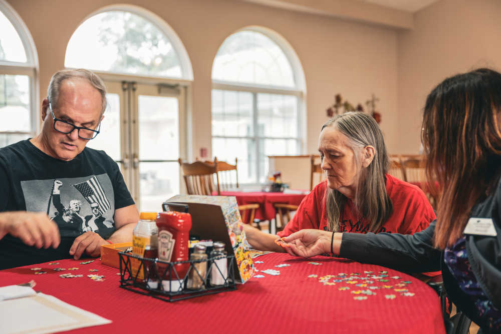 Three people working on a jigsaw puzzle at a table with condiments at Garden Place Millstadt in Millstadt, Illinois
