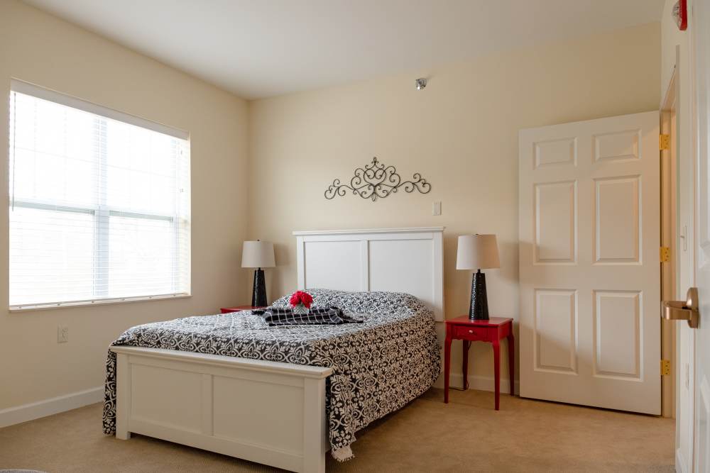 Bright bedroom with large window and night stand at The Harmony Collection at Roanoke - Assisted Living in Roanoke, Virginia