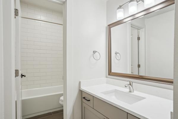 Modern washroom with large mirror and attached bathtub at Halston in Dallas, Texas