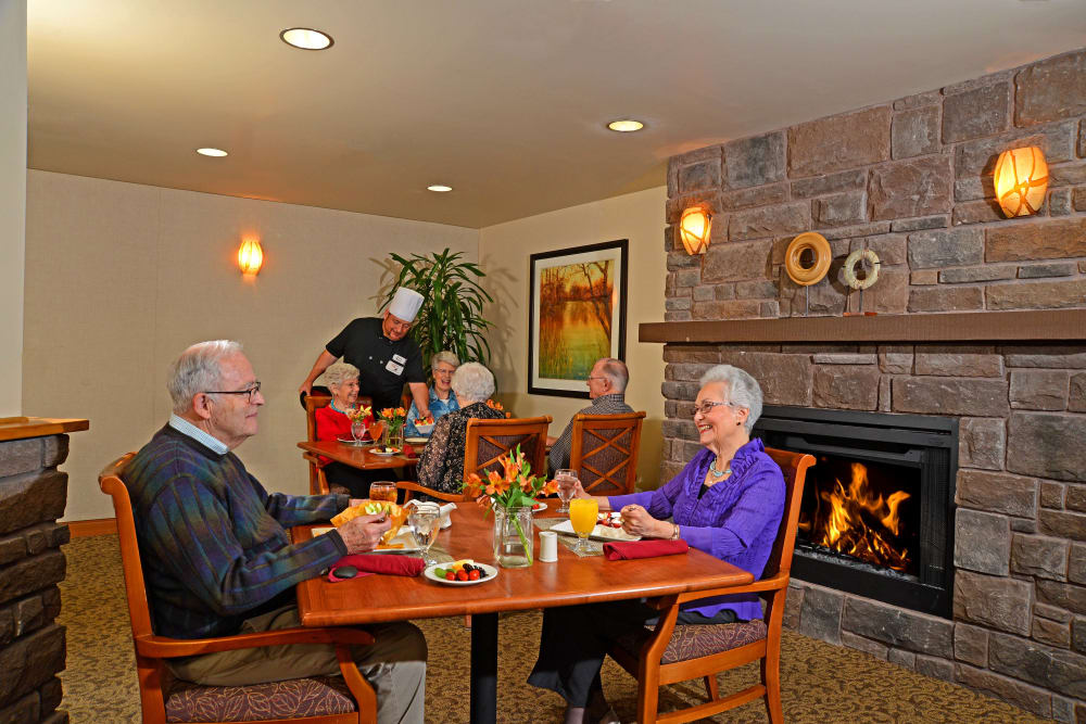 Residents sitting by a fireplace eating at Quail Park of Lynnwood in Lynnwood, Washington