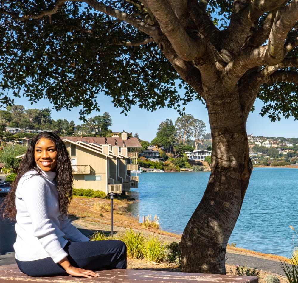 Resident sitting by a mature tree near the bay at Harbor Point Apartments in Mill Valley, California