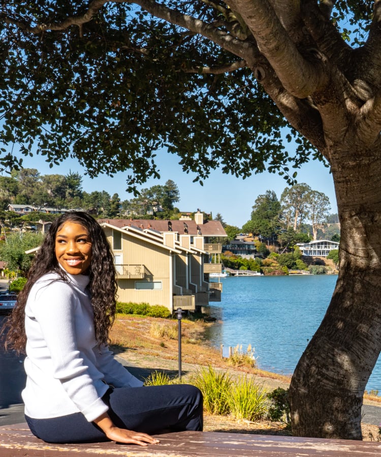 Resident sitting by a mature tree near the bay at Harbor Point Apartments in Mill Valley, California