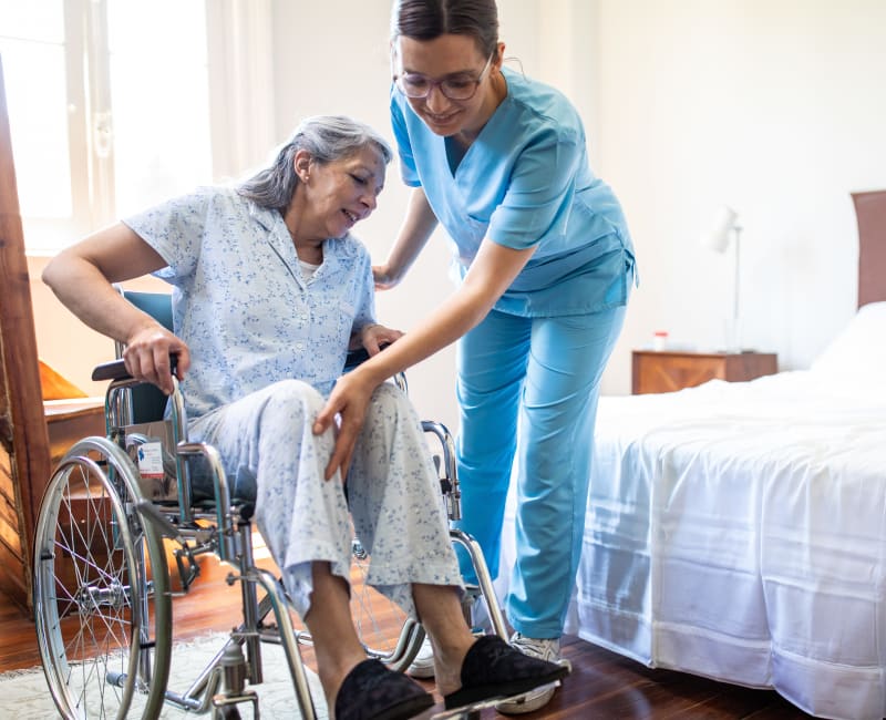 Caregiver helping a woman into her wheelchair in her apartment at Arbor Glen Senior Living in Lake Elmo, Minnesota