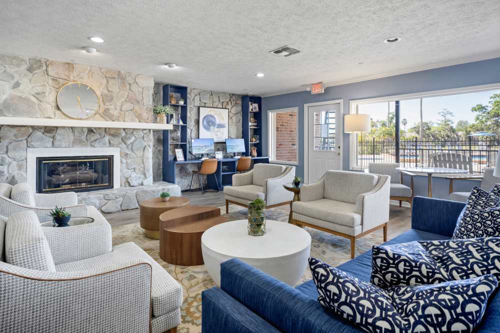 Modern clubhouse lounge with a stone fireplace, comfortable seating, a workspace area with computers, and large windows at Carlton Arms Of Magnolia Valley in New Port Richey, Florida