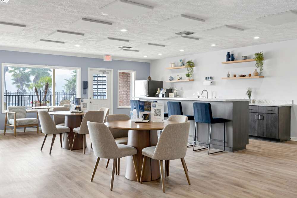 Bright community lounge with modern furniture, wood-style flooring, and kitchen area featuring stainless steel appliances at Carlton Arms North in Tampa, Florida
