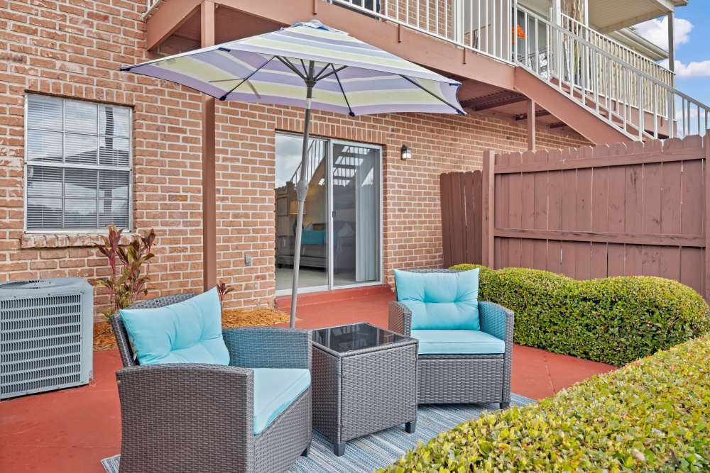 Cozy outdoor patio with two chairs, table, and umbrella, surrounded by greenery and brick wall at Carlton Arms North in Tampa, Florida