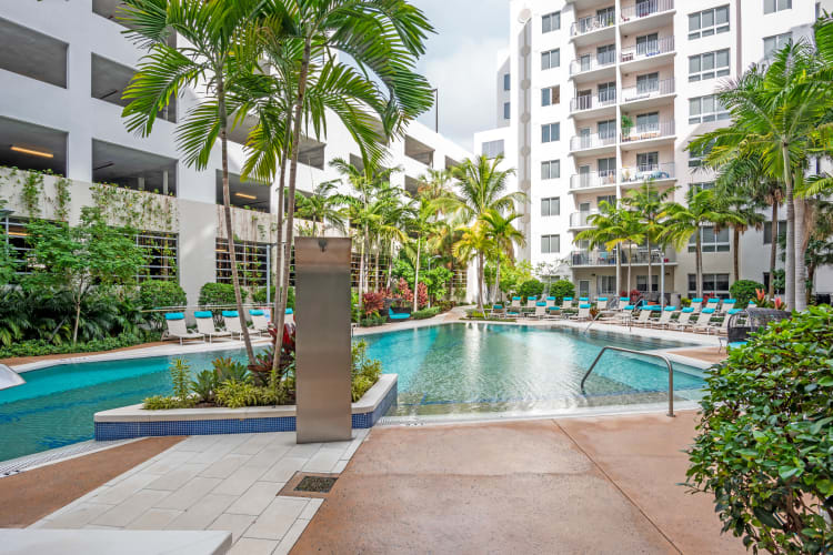 Swimming pool area surrounded by lush flora at Loftin Place Apartments in West Palm Beach, Florida