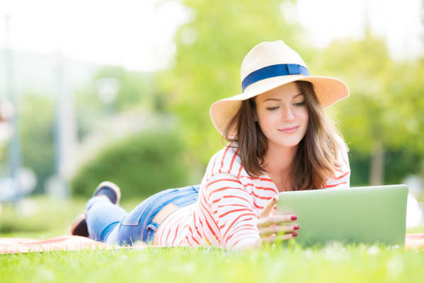 Smiling young woman lying on the grass and using her laptop near Warner Village Apartments in Trenton, New Jersey